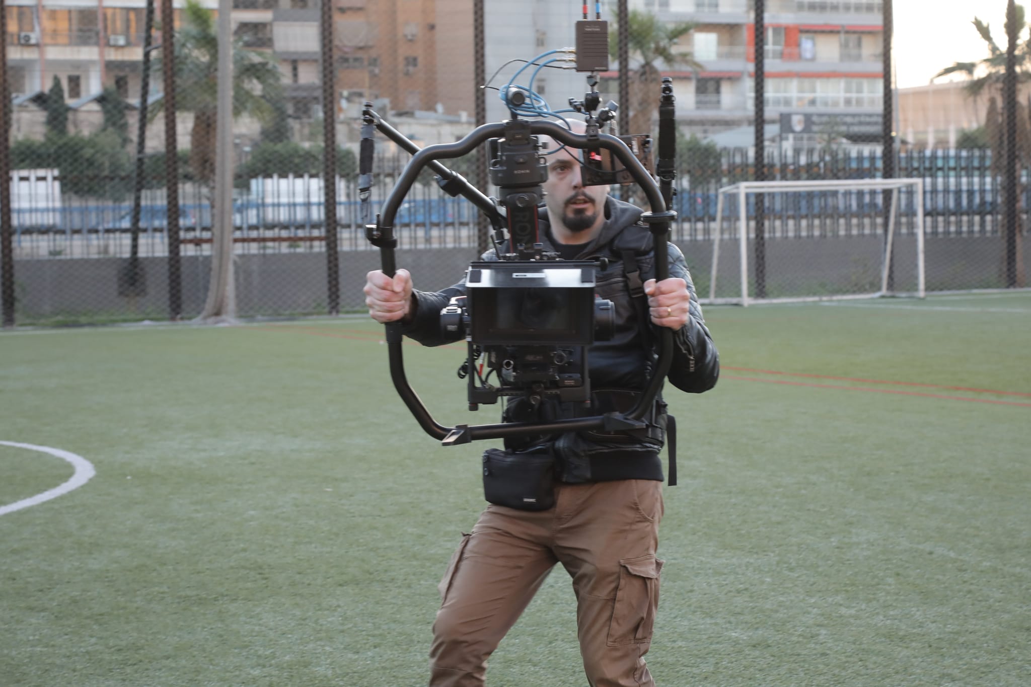 A camera operator carries a stabilised camera rig across a football pitch