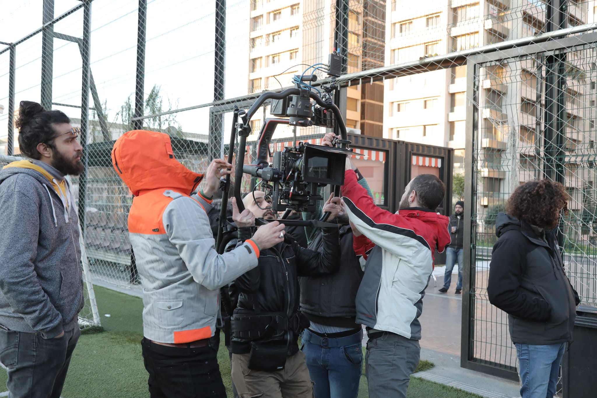 Crew members set up a stabilised camera rig beside a football pitch