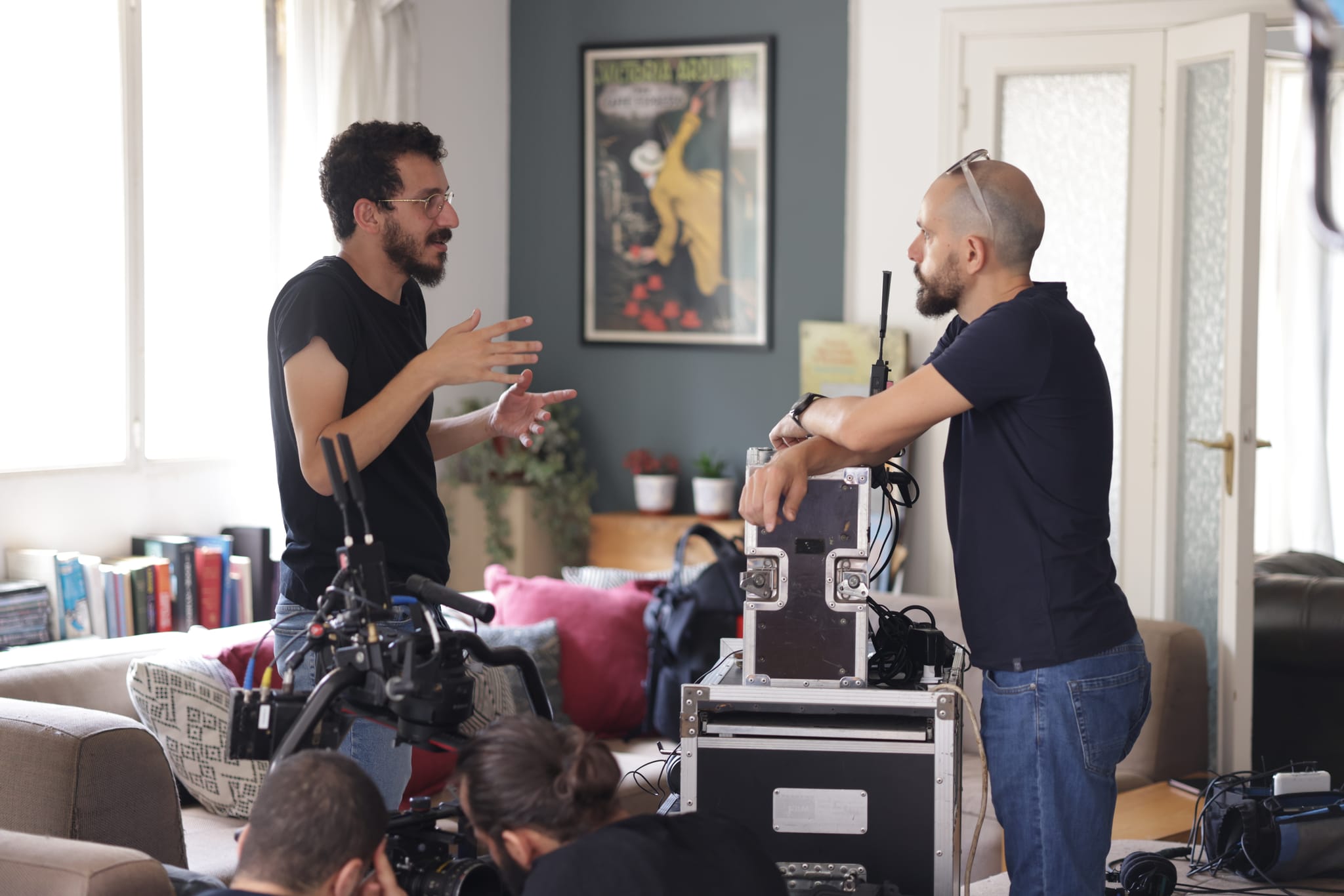 Two crew members talk through a shot beside the camera on a living-room set