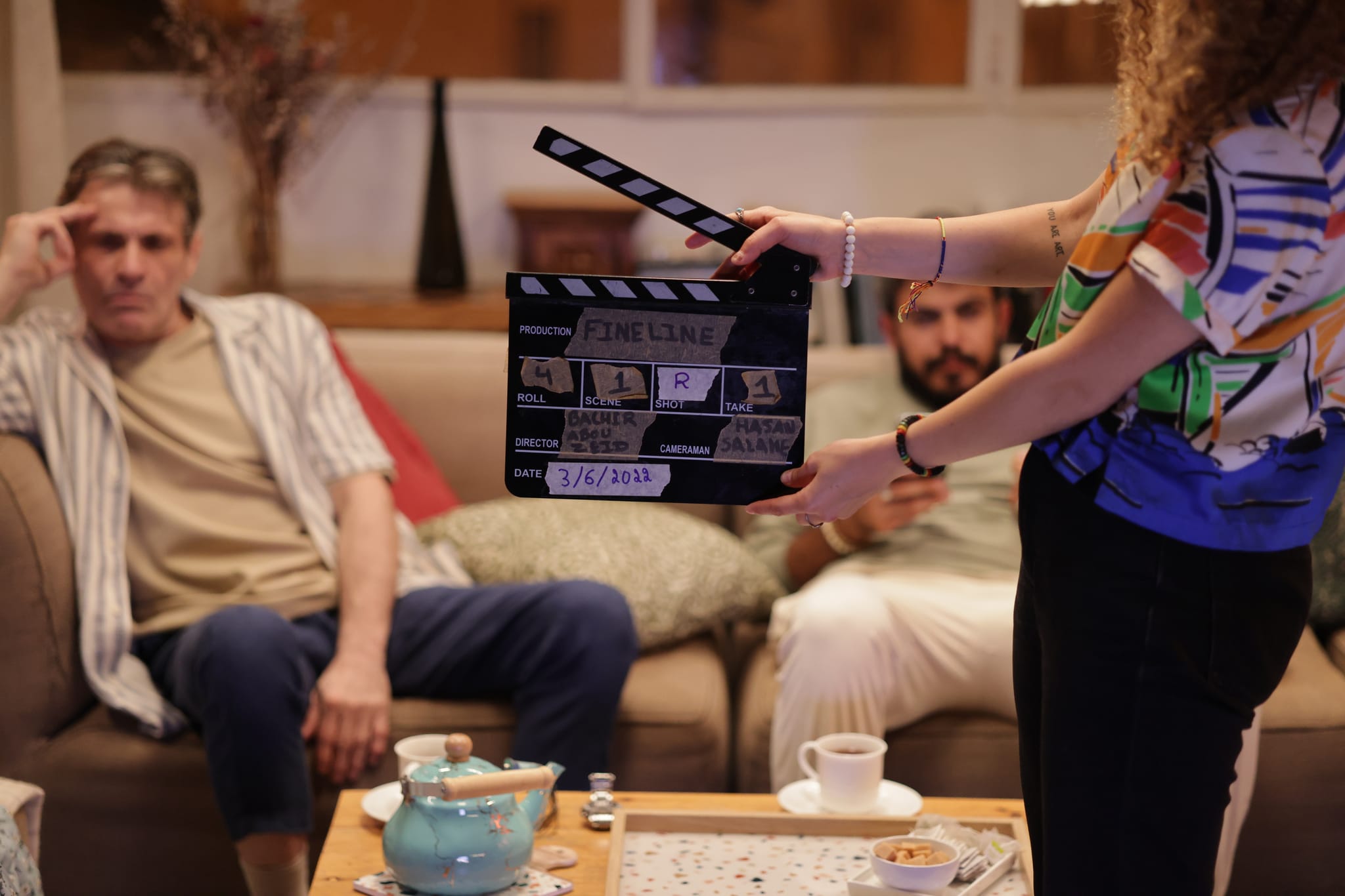A slate held in front of two actors seated on a sofa before a take