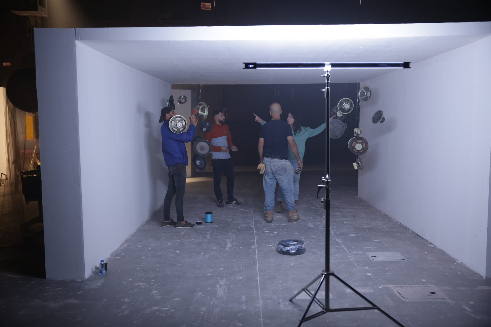 Crew members dress a white corridor set, with a light stand in the foreground