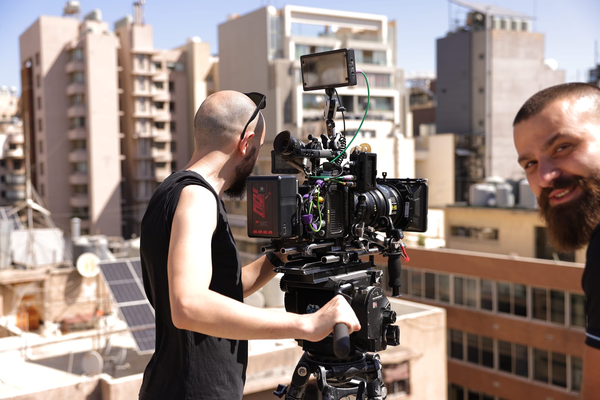 A camera operator with a cinema camera on a rooftop, with city buildings behind